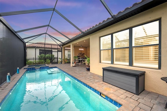 pool at dusk featuring a patio, glass enclosure, and an in ground hot tub