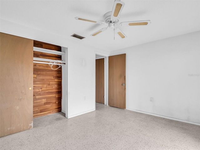 unfurnished bedroom featuring ceiling fan, wooden walls, and a closet