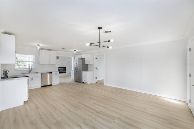 kitchen with pendant lighting, white cabinets, stainless steel appliances, ornamental molding, and light wood-type flooring