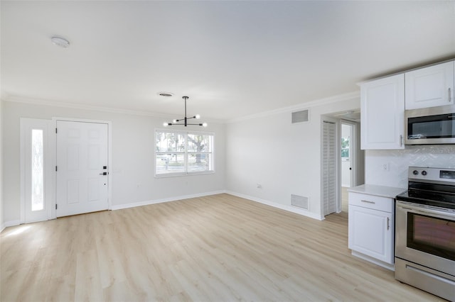 kitchen with white cabinetry, appliances with stainless steel finishes, crown molding, and a chandelier