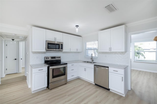 kitchen with sink, light wood-type flooring, appliances with stainless steel finishes, ornamental molding, and white cabinets