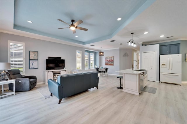 living room with ceiling fan, sink, a tray ceiling, ornamental molding, and light hardwood / wood-style floors