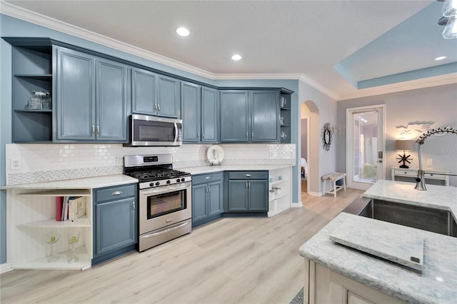 kitchen with appliances with stainless steel finishes, backsplash, blue cabinets, light stone counters, and light hardwood / wood-style floors