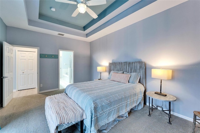 bedroom featuring ceiling fan, a raised ceiling, light carpet, and ensuite bath