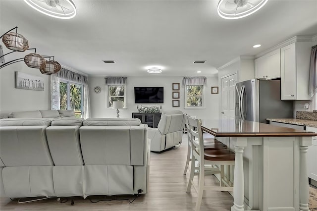 kitchen featuring white cabinetry, light hardwood / wood-style floors, stainless steel fridge with ice dispenser, a breakfast bar, and crown molding