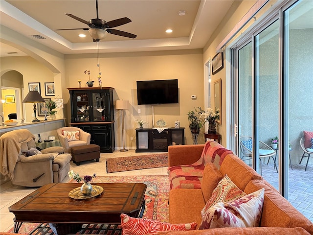 living room with light tile patterned floors, ceiling fan, and a tray ceiling