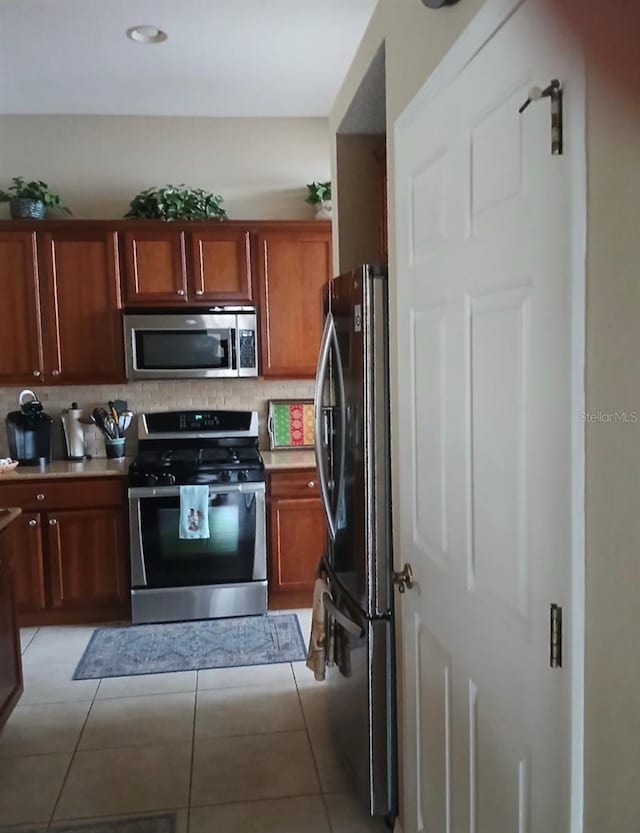 kitchen featuring stainless steel appliances, light countertops, light tile patterned flooring, and tasteful backsplash