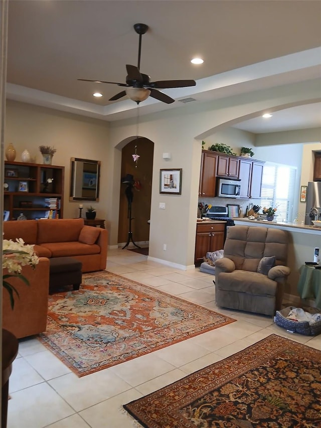 living area featuring arched walkways, light tile patterned floors, recessed lighting, a ceiling fan, and a tray ceiling