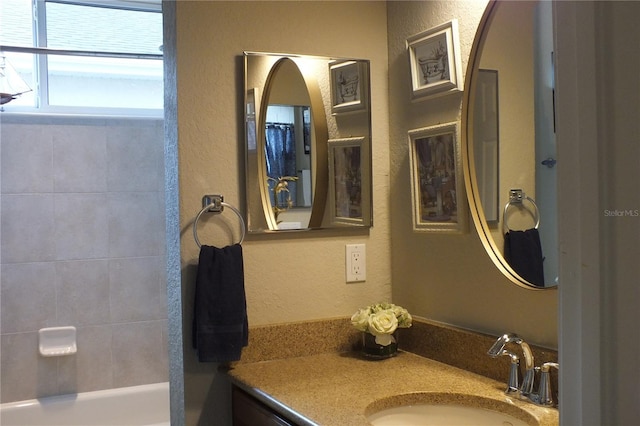 bathroom with a textured wall, washtub / shower combination, and vanity