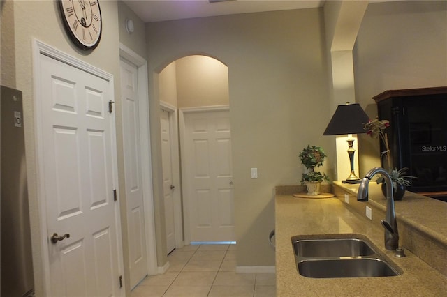 kitchen with arched walkways, light tile patterned floors, a sink, and baseboards