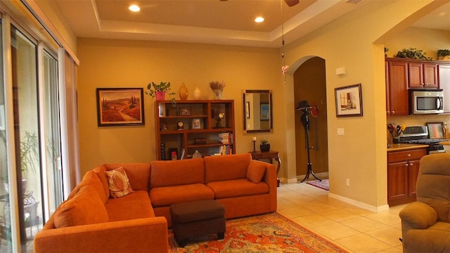 living area with arched walkways, a tray ceiling, light tile patterned floors, and baseboards