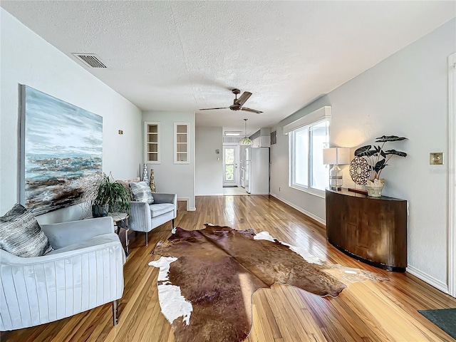 living room with ceiling fan, a textured ceiling, and light wood-type flooring