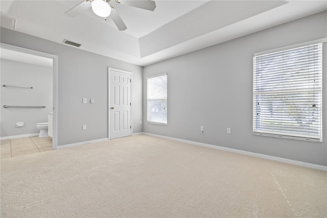 unfurnished bedroom with light carpet, ensuite bathroom, ceiling fan, a tray ceiling, and a closet