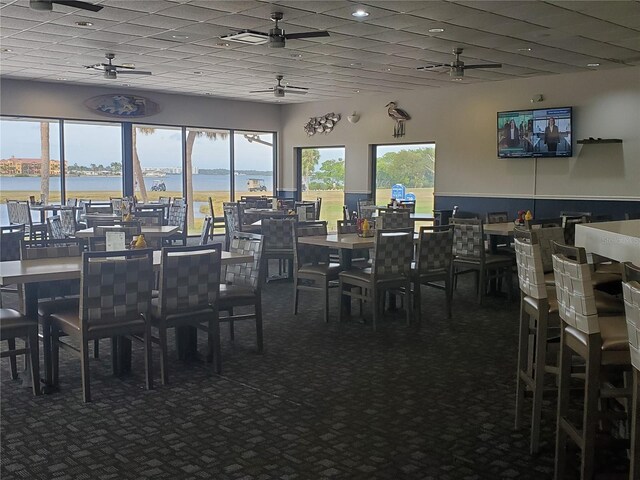 dining area with dark carpet, a water view, and a ceiling fan