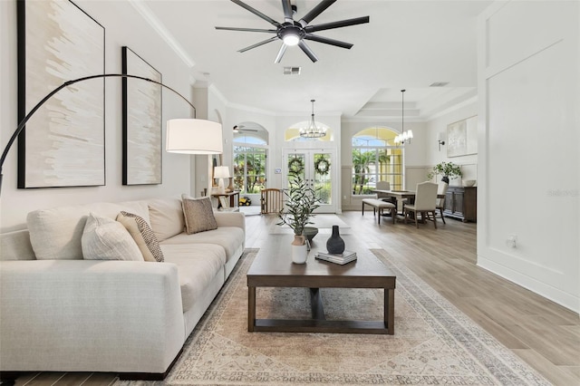 living room featuring ornamental molding, a notable chandelier, light hardwood / wood-style floors, and french doors