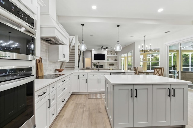 kitchen with black electric stovetop, custom range hood, white cabinets, decorative light fixtures, and kitchen peninsula