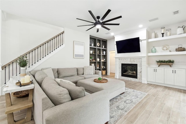 living room featuring a tile fireplace, ceiling fan, light hardwood / wood-style floors, and built in shelves