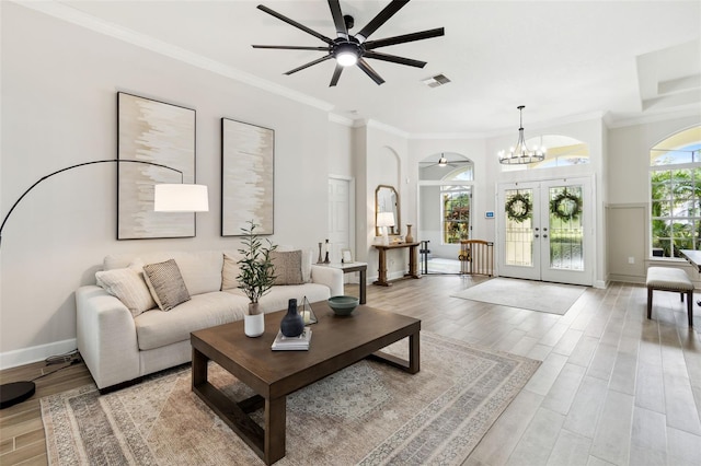 living room featuring ceiling fan with notable chandelier, light hardwood / wood-style flooring, ornamental molding, and french doors