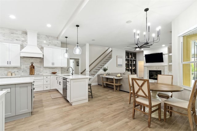 kitchen with sink, custom exhaust hood, decorative light fixtures, dishwasher, and white cabinets