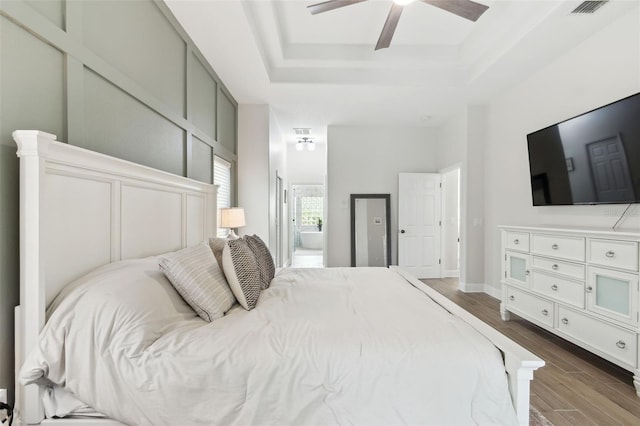 bedroom featuring ceiling fan, ensuite bath, dark hardwood / wood-style floors, and a raised ceiling