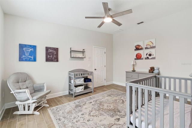 bedroom with wood-type flooring, a nursery area, and ceiling fan