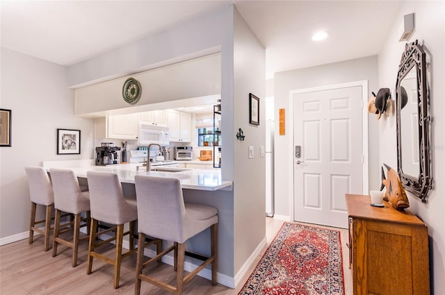 kitchen with a breakfast bar, sink, white cabinets, light hardwood / wood-style floors, and kitchen peninsula