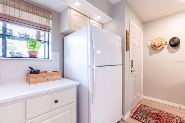 kitchen featuring white fridge, light stone counters, white cabinets, and light wood-type flooring