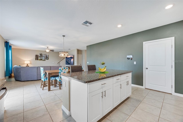 kitchen with dark stone countertops, a kitchen island, white cabinetry, and hanging light fixtures