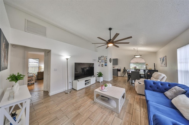 living room with ceiling fan, vaulted ceiling, and a textured ceiling