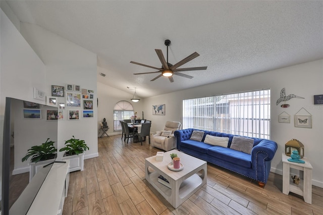 living room with a textured ceiling, ceiling fan, a wealth of natural light, and lofted ceiling