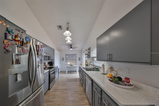 kitchen with decorative light fixtures, vaulted ceiling, sink, appliances with stainless steel finishes, and a textured ceiling