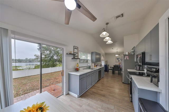 kitchen featuring stainless steel appliances, lofted ceiling, hanging light fixtures, a water view, and sink