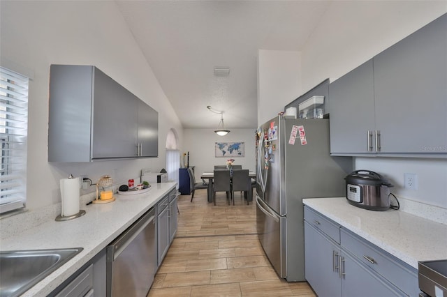 kitchen featuring lofted ceiling, hanging light fixtures, gray cabinetry, and stainless steel appliances