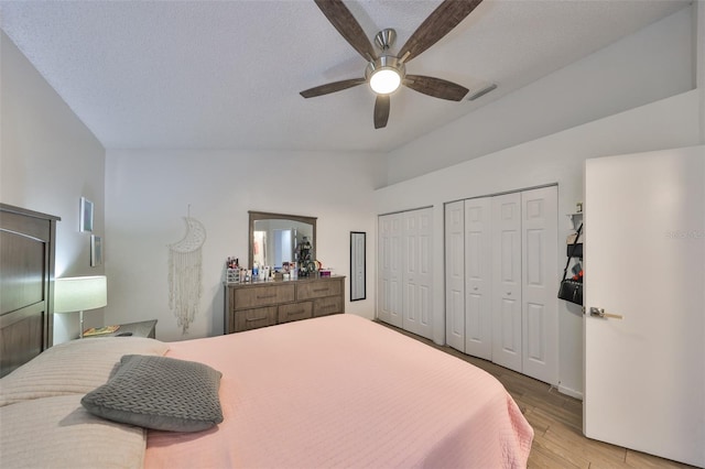 bedroom with ceiling fan, multiple closets, a textured ceiling, and light hardwood / wood-style floors