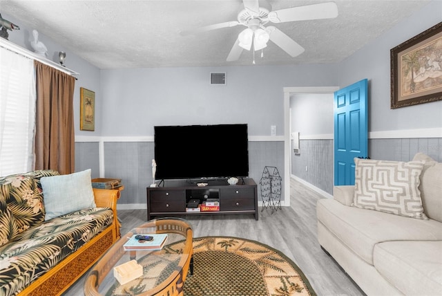 living room with ceiling fan, a textured ceiling, and light wood-type flooring