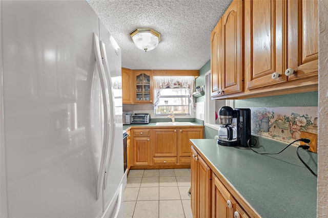 kitchen with light tile patterned floors, a toaster, freestanding refrigerator, a textured ceiling, and a sink