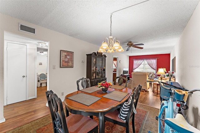 dining area with a textured ceiling, ceiling fan with notable chandelier, and wood-type flooring