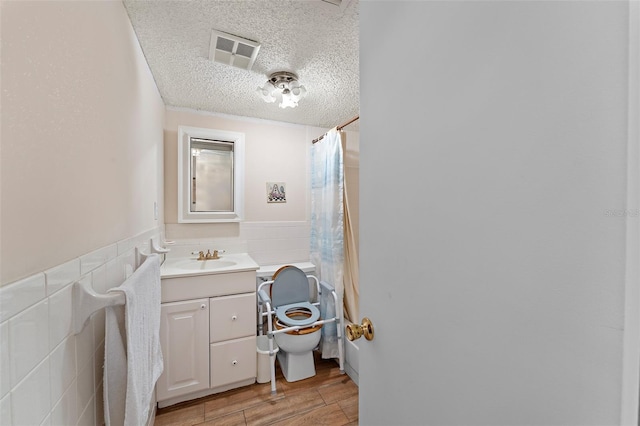 bathroom featuring tile walls, visible vents, toilet, wainscoting, and a textured ceiling