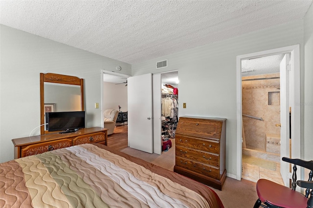 carpeted bedroom featuring a textured ceiling, a closet, a walk in closet, and visible vents