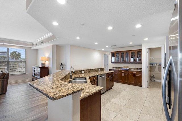 kitchen with a spacious island, glass insert cabinets, freestanding refrigerator, crown molding, and a sink