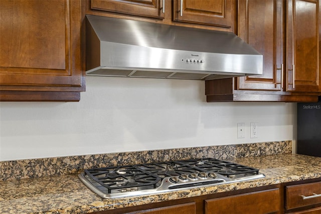 kitchen featuring under cabinet range hood, stainless steel gas stovetop, and dark stone counters