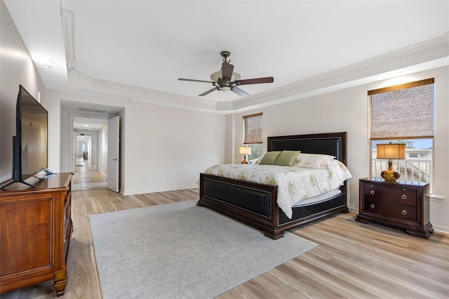 bedroom with light wood finished floors, baseboards, a raised ceiling, ceiling fan, and crown molding