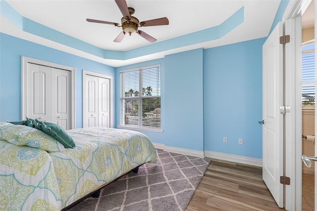 bedroom with two closets, a raised ceiling, ceiling fan, wood finished floors, and baseboards