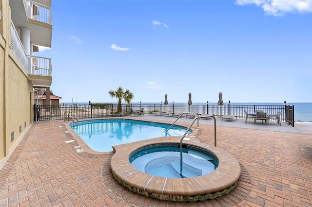 community pool featuring a water view, a patio area, fence, and a community hot tub