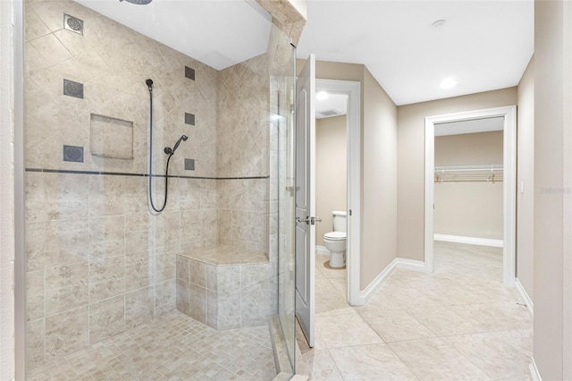 bathroom with tile patterned flooring, toilet, baseboards, a shower stall, and a walk in closet