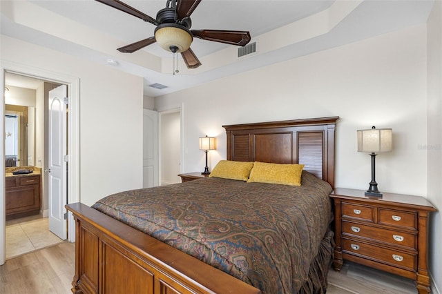 bedroom with a tray ceiling, light wood-type flooring, connected bathroom, and visible vents