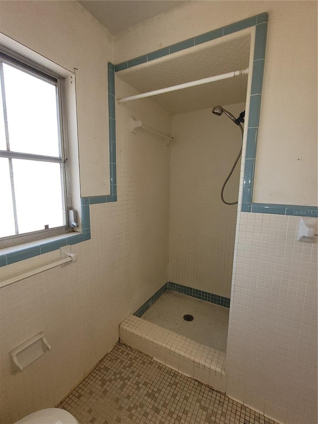 bathroom featuring tile walls, tile patterned flooring, toilet, and tiled shower