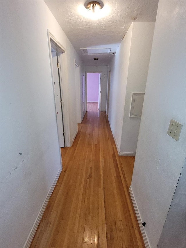 hall with a textured ceiling and light wood-type flooring