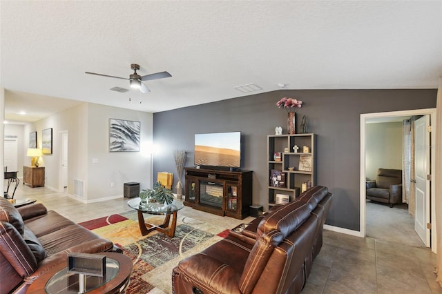 living room featuring a textured ceiling, a fireplace, light tile patterned floors, ceiling fan, and lofted ceiling