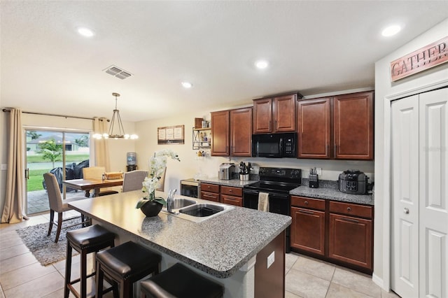 kitchen featuring black appliances, light tile patterned floors, sink, an island with sink, and a breakfast bar area